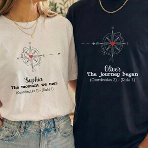 May include: White and black t-shirts with a compass design and text. The white shirt says "Sophia, The moment we met" and the black shirt says "Oliver, The journey began". Both shirts have a red heart in the center of the compass.