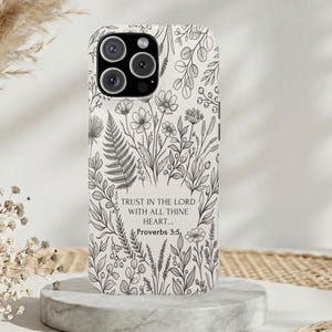 May include: A white smartphone case featuring a black line art botanical pattern of various wildflowers, ferns, and leaves. Centered on the case is the text, Trust in the Lord with all thine heart... Proverbs 3:5, printed in a simple black font.