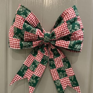 Può includere: Un grande fiocco decorativo con un design patchwork. Il fiocco presenta quadrati alternati di tessuto a quadretti rosso e bianco e verde con un motivo floreale. Probabilmente per decorazioni stagionali o festive.