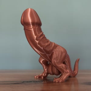 Könnte beinhalten: Eine 3D-gedruckte Figur in metallischer Kupferoptik, die ein Wesen mit phallisch geformtem Kopf und Oberkörper darstellt, auf zwei Hinterbeinen mit Schwanz steht und sichtbare horizontale Schichtlinien des Druckprozesses aufweist.