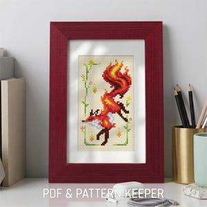 May include: A framed cross-stitch of a fox with a fiery tail, in shades of red, orange, and yellow. The fox is set against a cream-colored background with floral accents. The frame is a deep red color. Text at the bottom reads "PDF & PATTERN KEEPER."