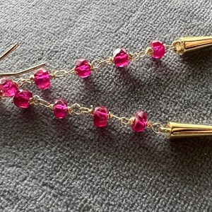May include: A pair of long, dangling earrings with a gold chain and pink faceted beads. The earrings have a gold spike at the bottom.