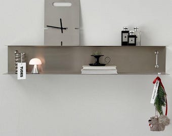 May include: A modern, minimalist wall shelf with a gray finish, holding a small lamp, books, and decorative items. A gray clock hangs above the shelf. A Christmas ornament with a squirrel is hanging from the shelf.