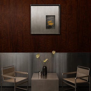 May include: Two metal chairs with light-colored fabric seats and backrests flank a square metal side table. On the table sits a dark vase with three yellow flowers and a small metal cup. A square metal-framed artwork hangs on the wall above.
