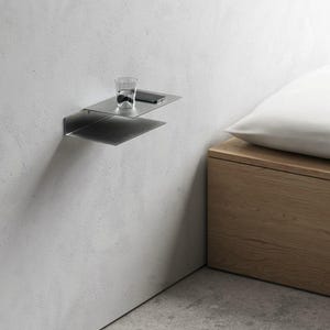 Peut inclure: Étagère flottante en métal moderne et minimaliste fixée à un mur blanc. Un verre transparent et un smartphone reposent sur l'étagère supérieure. Une table de chevet en bois et un oreiller blanc sont en arrière-plan.