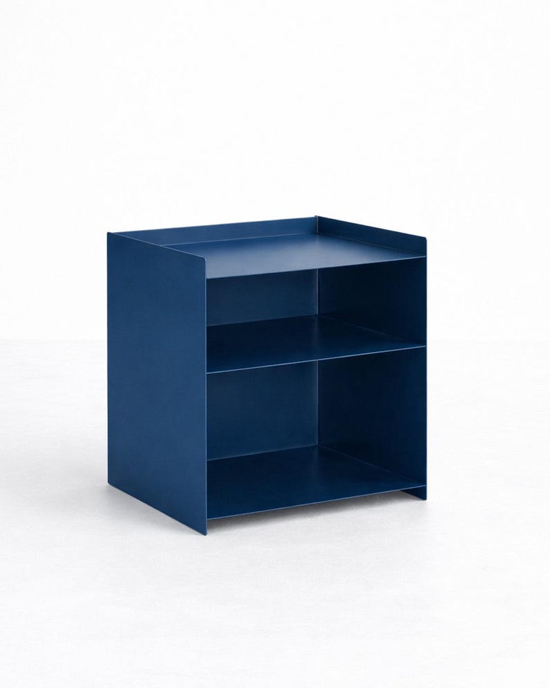 Puede incluir: Una unidad de almacenamiento de metal azul oscuro con un marco cuadrado, dos estantes abiertos y un borde elevado a lo largo de la superficie superior. La estructura est&aacute; compuesta por paneles planos y delgados con un acabado mate.