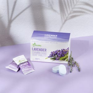 May include: A box of lavender foaming hand soap tablets with a sprig of lavender. The box is white and purple with the words "Lavender Foaming Hand Soap Tablets" printed on it. Two individual soap tablets and two packets are also visible.