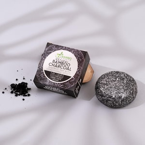 May include: A black and grey shampoo bar with the text "Natural Bamboo Charcoal" and a box with the same text. The bar is round and has a conditioning effect. A small pile of charcoal is next to the bar.