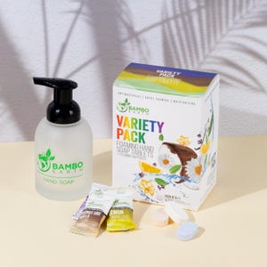 May include: A frosted glass hand soap dispenser with a black pump, next to a box of foaming hand soap tablets. The box is labeled "Variety Pack" and features a coconut and floral design. Individual soap tablets and sample packets are also visible.