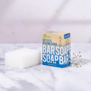 Peut inclure: Un pain de savon rectangulaire blanc et non parfumé à côté d'une boîte de savon en barre pour la vaisselle naturelle. La boîte est bleue et beige avec les mots "BAR SOAP BARS" en grandes lettres blanches. La boîte indique "Unscented".