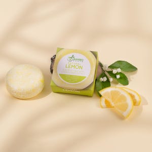May include: A yellow, round shampoo bar and a boxed shampoo bar with the text "Natural Lemon" and "Shampoo Bar with Conditioning Effect". The image also includes lemon slices and leaves, all on a light yellow background.