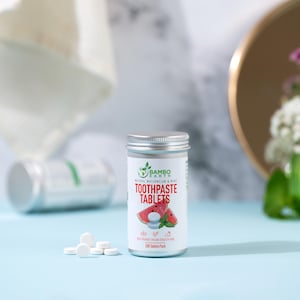 May include: A silver metal container of "Bambo Earth" toothpaste tablets with a watermelon and mint flavor. The label features watermelon slices and the text "Toothpaste Tablets". Several white tablets are scattered in front of the container.