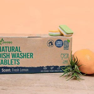 May include: A cardboard box of "Bambo Earth Natural Dish Washer Tablets" with "Fresh Lemon" scent. Two dish scrubbers and a lemon sit on a wooden surface. The box has green and blue text and logos.