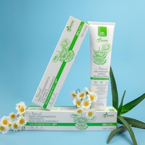 May include: A white tube and boxes of natural toothpaste with green accents, aloe vera, and chamomile. The packaging features the brand name "Bambo Earth" and the text "Great for Sensitive Teeth". The image includes a sprig of daisies and aloe vera leaves.