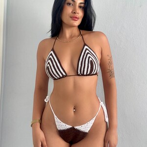 Può includere: Un set bikini all'uncinetto marrone e bianco. La parte superiore presenta un design all'americana con strisce verticali e la parte inferiore è un perizoma con blocchi di colore abbinati. Il bikini è legato con cordini bianchi.