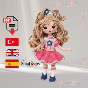 Puede incluir: Muñeca de ganchillo hecha a mano con pelo largo y rizado castaño y un vestido rosa. La muñeca tiene un top azul y blanco, zapatos azules y calcetines blancos. La imagen incluye un icono PDF, banderas turcas, británicas y españolas, y el texto "ShiaLoops".
