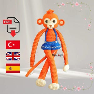 May include: A handmade orange crochet monkey doll with long arms and legs. The monkey wears a blue skirt with suspenders and has white accents on its hands and feet. The doll has a round head with large eyes and ears. The text "ShiaLoops" is visible.