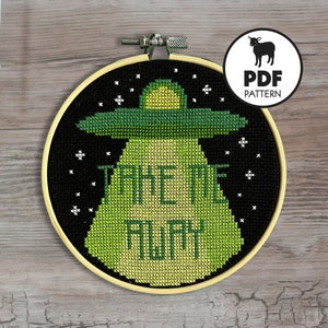May include: A black and green cross-stitch embroidery hoop with a UFO and the text "Take the Awful Away".