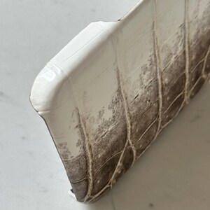 May include: Close-up of a white and brown textured phone case. The case has a glossy finish and a pattern that resembles crocodile skin. The case is curved at the top and has a dark brown color on the bottom.