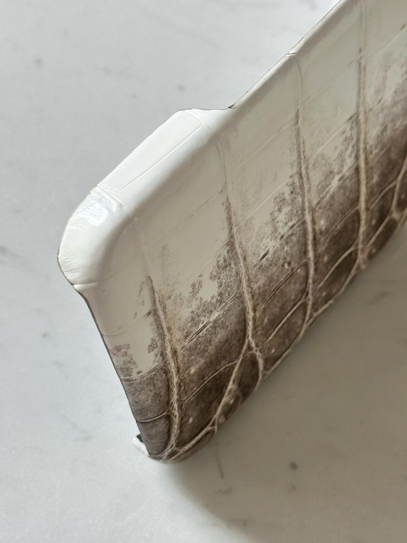 May include: Close-up of a white and brown textured phone case. The case has a glossy finish and a pattern that resembles crocodile skin. The case is curved at the top and has a dark brown color on the bottom.