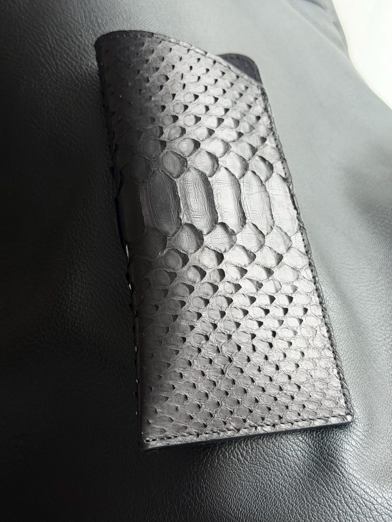 Pu&ograve; includere: Un portafoglio nero rettangolare con un motivo squamoso strutturato. Il portafoglio sembra essere in pelle e ha una chiusura a patta. Il design generale &egrave; elegante e moderno, adatto per trasportare carte e contanti.