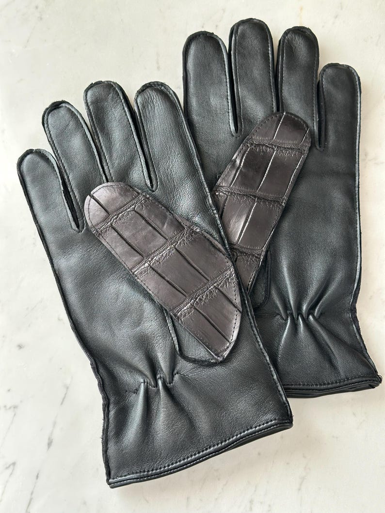 Pode incluir: Um par de luvas de couro preto com um remendo texturizado marrom escuro na palma da m&atilde;o. As luvas s&atilde;o feitas de couro liso e t&ecirc;m um design cl&aacute;ssico, adequado para o clima frio.
