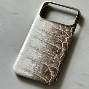 May include: A white and brown crocodile-textured phone case. The case has a rectangular shape with rounded corners and a cutout for the camera. The color transitions from white to brown, with a textured pattern.