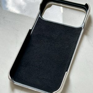 May include: A white and black phone case with a soft, black interior. The case has a raised edge around the camera and screen openings. The case is designed to protect the phone from scratches and damage.