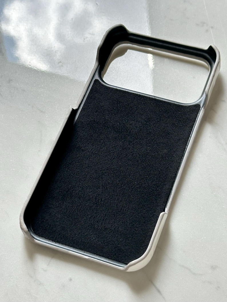 May include: A white and black phone case with a soft, black interior. The case has a raised edge around the camera and screen openings. The case is designed to protect the phone from scratches and damage.