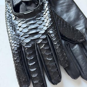 May include: Black leather gloves with a snakeskin pattern on the back of the hand and fingers. The gloves have a snap closure at the wrist and are made of a soft, supple leather.