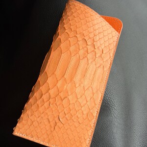 Pu&ograve; includere: Un astuccio per occhiali arancione con texture di pelle di serpente e interno arancione. La custodia &egrave; rettangolare con un bordo cucito. La custodia &egrave; realizzata in un materiale simile alla pelle di serpente.