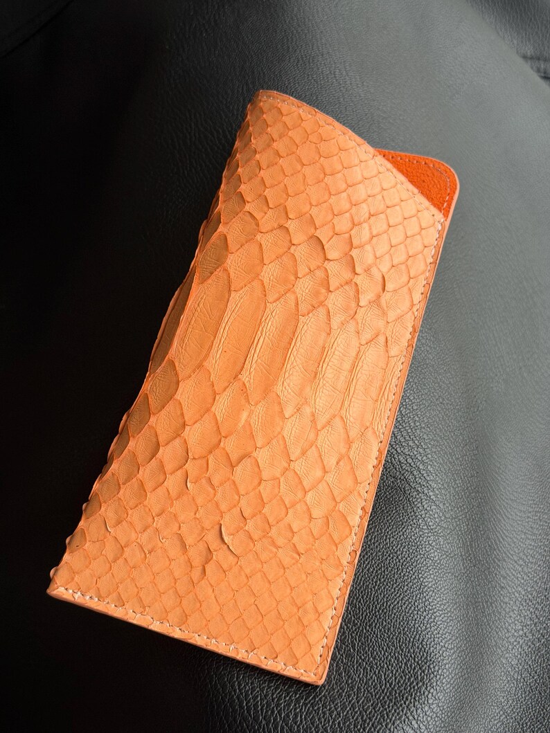 Pu&ograve; includere: Un astuccio per occhiali arancione con texture di pelle di serpente e interno arancione. La custodia &egrave; rettangolare con un bordo cucito. La custodia &egrave; realizzata in un materiale simile alla pelle di serpente.
