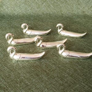May include: Six silver swan-shaped chopstick rests. The rests are arranged on a green textured surface. Each swan has a curved neck and a streamlined body, adding a touch of elegance to any dining setting.