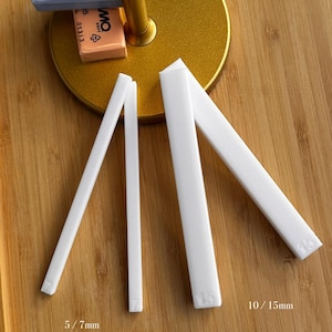 Könnte beinhalten: Weiße Kunststoff-Modellierwerkzeuge, darunter Größen von 5/7 mm und 10/15 mm, werden auf einer Holzoberfläche gezeigt. Zwei Blöcke FIMO SOFT-Ton, einer blau und einer orange, mit Produktdetails.