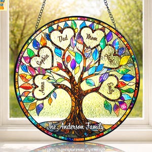 May include: A round, stained-glass family tree with a black border and chain for hanging. The tree features colorful leaves and heart-shaped spaces with names like "Dad," "Mom," and others. The words "The Anderson Family" are at the base.