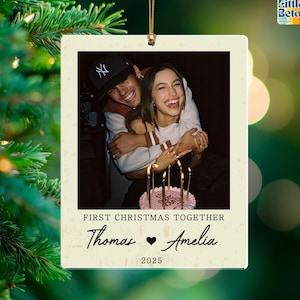 May include: A personalized Christmas ornament featuring a photo of a smiling couple embracing. The ornament has the text "First Christmas Together" and the names "Thomas ♥ Amelia" with the year "2025" below. The ornament is rectangular with a gold string.