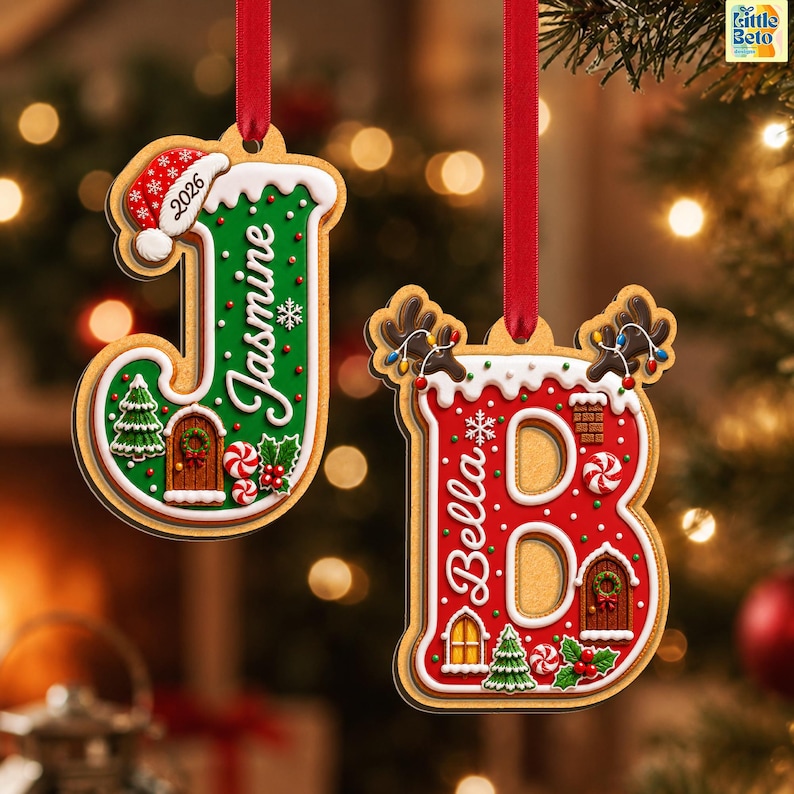 May include: Two hanging Christmas ornaments shaped like the letters J and B. The J is green with a Santa hat and the name Jasmine. The B is red with reindeer antlers and the name Bella. Both feature white icing, trees, doors, and red ribbons.