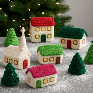 Può includere: Una collezione di decorazioni natalizie fatte a mano all'uncinetto, tra cui case con tetti rossi, verdi e rosa, una chiesa e alberi di Natale verdi. Le case hanno cornici di finestre e porte gialle. La scena è ambientata su uno sfondo sfocato di albero di Natale.