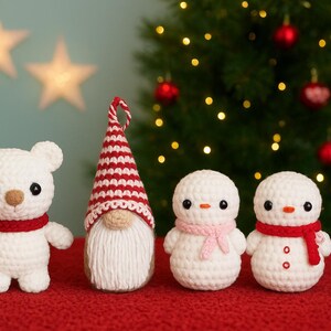Könnte beinhalten: Eine Sammlung handgefertigter Weihnachtsornamente aus Häkelarbeit. Enthält einen weißen Bären mit rotem Schal, einen Wichtel mit roter und weißer Mütze und zwei Schneemänner mit Schals. Im Hintergrund ein Weihnachtsbaum mit Lichtern und Kugeln.