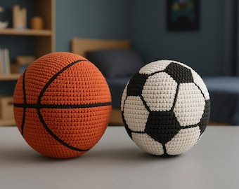 May include: Two crocheted sports balls: an orange basketball with black lines and a soccer ball with black and white pentagons. The balls are handmade and sit on a gray surface, suggesting a playful theme.