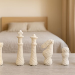 Puede incluir: Un conjunto de seis piezas de ajedrez blancas, que incluyen una torre, una reina, un rey, un caballo, un peón y un alfil, están dispuestas sobre una superficie clara. Las piezas tienen un patrón texturizado y punteado. El fondo incluye una cama y una mesita de noche.