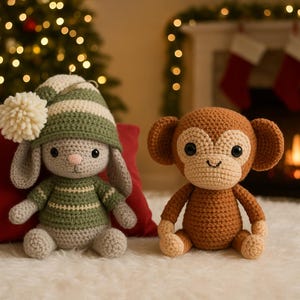 Op de afbeelding: Twee handgemaakte gehaakte knuffels: een konijn met een groen-witte gestreepte muts en trui, en een bruine aap. Het konijn heeft een crèmekleurige pompon op zijn muts. Ze zitten op een witte, zachte ondergrond.