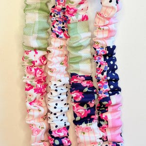 May include: Four long, fabric-covered elastic bands arranged vertically. Each band features a patchwork design of various patterns including pink roses, green gingham checks, navy blue polka dots, and thin pink stripes on a white background.