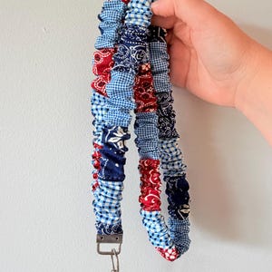 Op de afbeelding: Een stoffen lanyard met een patchworkontwerp van rode en marineblauwe paisley-bandanapatronen gecombineerd met lichtblauwe en witte gingham-ruitjes. De band is geplooid met elastiek en voorzien van een zilverkleurige metalen draaibare karabijnhaak.