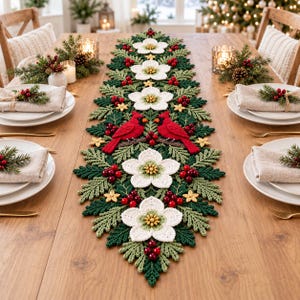 Puede incluir: Un camino de mesa de ganchillo largo y rectangular con un diseño central de dos pájaros cardenales rojos posados en ramas, rodeados de flores blancas, agujas de pino verdes, hojas de acebo y racimos de pequeñas bayas rojas.