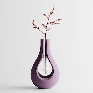 Könnte beinhalten: Eine moderne, tropfenförmige Vase in einem gedämpften Lila. Die Vase hat ein klares Glasrohr zur Aufnahme von Wasser und einen schlanken Zweig mit kleinen, braunen Blättern. Das Design ist minimalistisch und elegant, geeignet für die Inneneinrichtung.