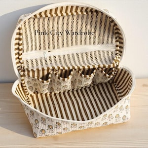 May include: Open, oval cosmetic bag with a white zip and interior pockets. The bag has a striped brown and white interior and a floral patterned exterior. The text "Pink City Wardrobe" is visible on the inside.