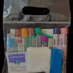 May include: A clear plastic bag containing medical supplies. The kit includes vials with colored caps, alcohol prep pads, adhesive bandages, a white gauze pad, and a blue plastic item. The bag has a handle.