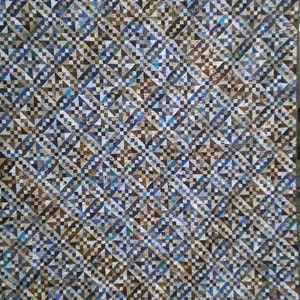 May include: A quilt made of patchwork squares in shades of blue, brown, and white. The squares are arranged in a geometric pattern, creating a visually interesting and intricate design.
