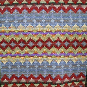 Puede incluir: Una colcha colorida con un patrón geométrico en tonos de rojo, azul, verde y amarillo. La colcha está hecha de tela de patchwork y tiene un diseño tradicional.